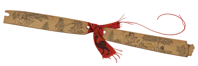 A strip of palm leaf with incised figures, tied with red thread.